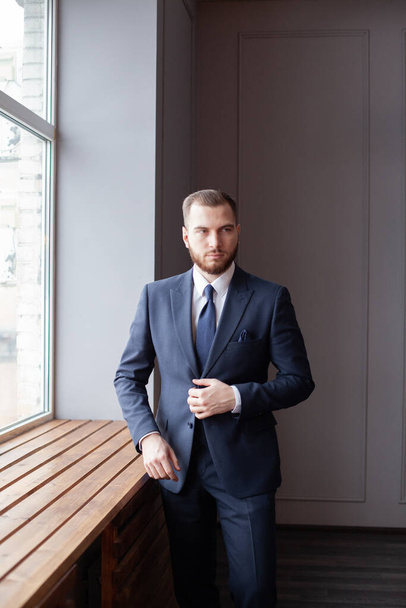 Портрет серьезного умного бизнесмена в костюме, стоящего в своем кабинете - Фото, изображение