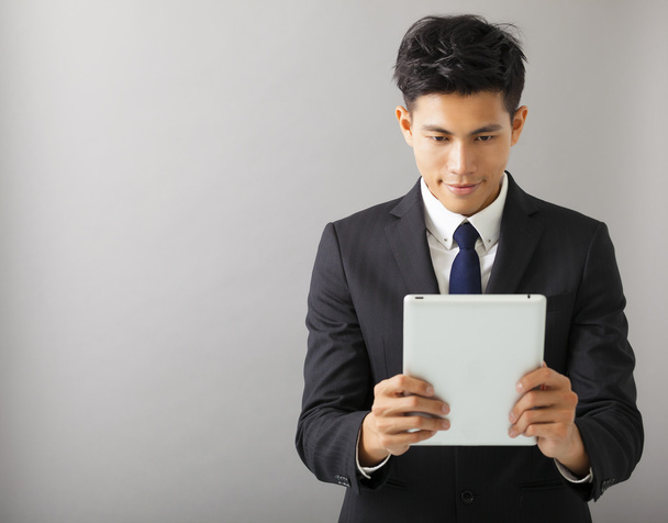 Junger lächelnder Geschäftsmann schaut auf den Tablet-PC - Foto, Bild