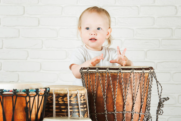 Carino bambino bambino che suona tamburi etnici accanto al muro mattoni - Foto, immagini