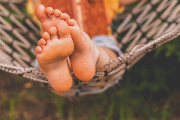 A young beautiful girl lies in a hammock and reads a book.  Selective focus on feets. Horizontal image. - Foto, Imagem