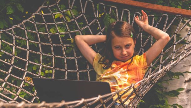 Huppy jong meisje werken op afstand met laptop buiten in een hangmat. - Foto, afbeelding
