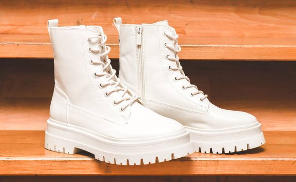 White demi-season boots made of eco-leather with fasteners, laces and rough soles stand on wooden steps, close-up side view. The concept of fashion and women's shoes. - Photo, Image