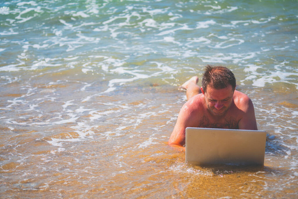 Empresário deitado na água do mar e trabalhando com laptop. Imagem horizontal. - Foto, Imagem