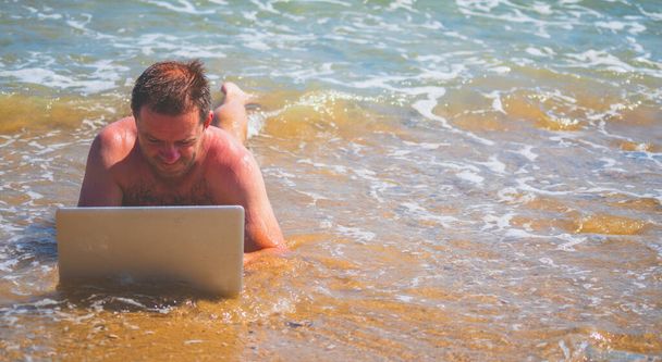 Homme d'affaires couché dans l'eau de mer et travaillant avec un ordinateur portable. Espace de copie pour la conception ou le texte.  - Photo, image