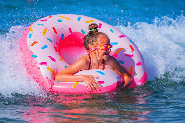 Joyful happy child girl on inflatable ring riding on breaking wave. Travel, healthy lifestyle and summer holiday concept.  - Foto, Imagen