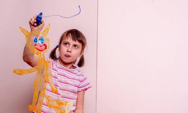 Beautiful young girl painting with fingers on the glass  red cat and blue sky. Copy space. - Photo, Image