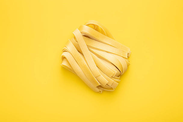 Uncooked pappardelle pasta on yellow background. Top view. - Fotoğraf, Görsel
