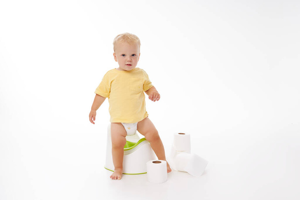 Potty training a baby. Little boy sitting on a potty next to a roll of toilet paper and diapers on a white background - Фото, зображення