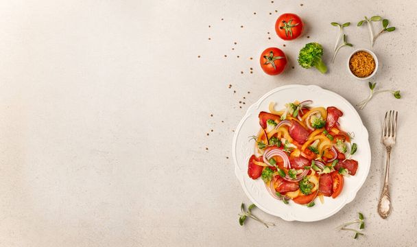 Salad with Prosciutto, tomatoes, onion, sweet pepper and broccoli. Cold snacks. Top view. Free space for your text. Tasty salad - ham, and fresh vegetables on stone background - Foto, imagen