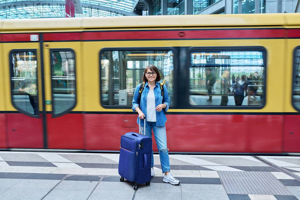 Woman with backpack suitcase at railway station. Female passenger with luggage on platform against background of train. Passenger transport, transportation, trip, journey, travel, people concept - Fotó, kép