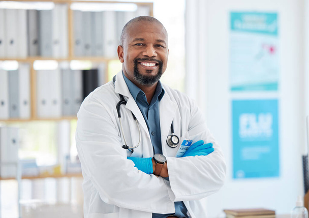Proud confident young doctor in his office. African american doctor arms crossed in his hospital. Happy medical gp standing in his office. Medical specialist in his clinic office. - Photo, image