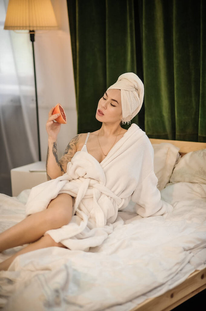 beautiful young woman in bathrobe and white robe lying on bed in bedroom - Photo, Image