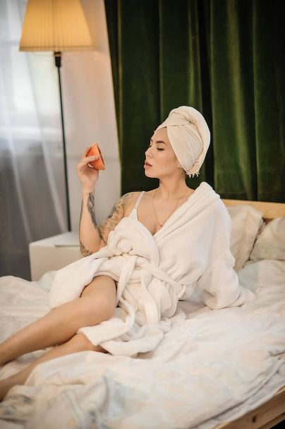 belle jeune femme en peignoir et serviette blanche assise sur le lit dans la chambre - Photo, image