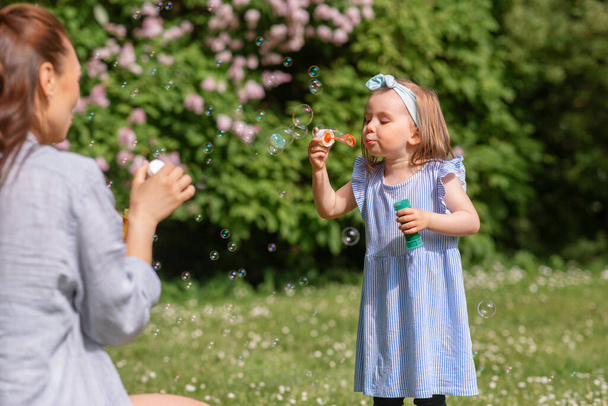 childhood, leisure and people concept - little girl with mother blowing soap bubbles at summer park or garden - 写真・画像