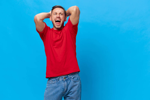Насолоджуючись веселим щасливим засмаглим красивим чоловіком у червоній футболці, піднімайте руки сміхом, позуючи ізольовано на синьому студійному фоні. Копіювати пробіл Банерний макет. Люди емоції Концепція способу життя - Фото, зображення