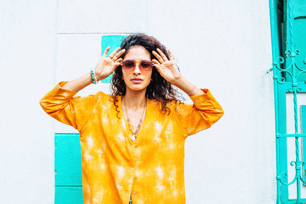 красива жінка з помаранчевою сорочкою і окулярами в місті з фоновою стіною влітку дивлячись на камеру, літній спосіб життя в місті
. - Фото, зображення