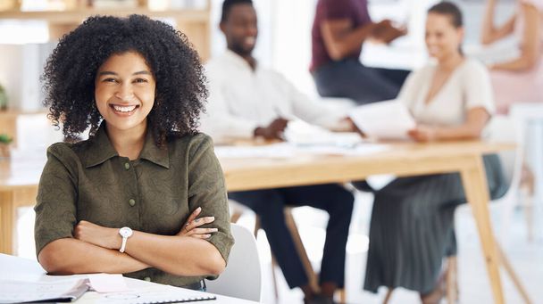 Happy mixed race businesswoman sitting with her arms crossed in an office at work. Confident female businessperson with a curly afro smiling while sitting at a table at work. - Foto, Bild