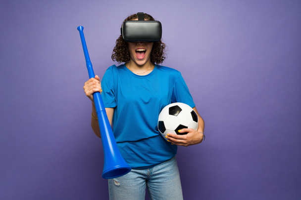 Cheerful female sports fan cheering for her favorite team while watching the soccer cup with virtual reality glasses  - Foto, imagen