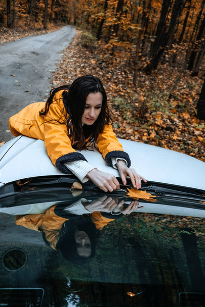 Pewna siebie brunetka stojąca w pobliżu samochodu i robiąca selfie na komórce. Jesienny weekend, wycieczka. Podróżuje samochodem. Piękno natury. - Zdjęcie, obraz