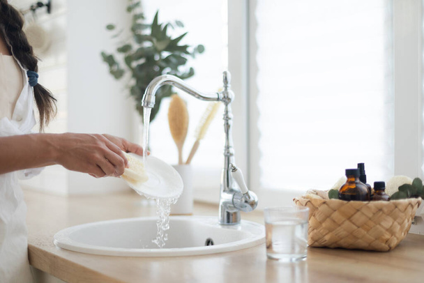 Kobieta zmywa naczynia detergentem w kuchni. Eko szczotka z pianką i kosz na białej jasnej kuchni - Zdjęcie, obraz