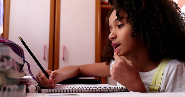 Little girl studying at home, mixed race child writing notes doing homework - 写真・画像