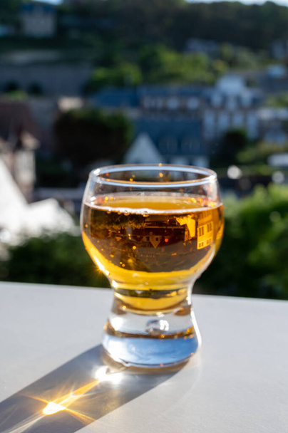 Un bicchiere di sidro di mele alla luce del sole e le case del villaggio Etretat sullo sfondo, Normandia, Francia - Foto, immagini