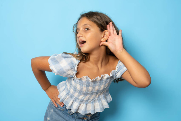 Little girl trying to hear you overhear listening intently isolated on blue background child studio portrait. Mother's Day love family people lifestyle concept - Foto, Imagem