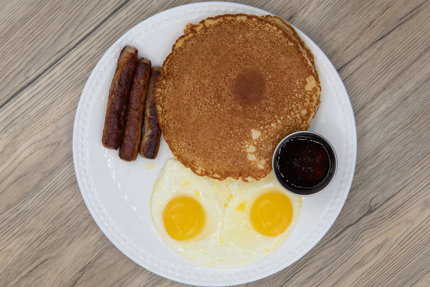 Overhead view of standard American breakfast consisting of pancakes, fried eggs, and sausage will ensure that the belly will be full. - Photo, Image