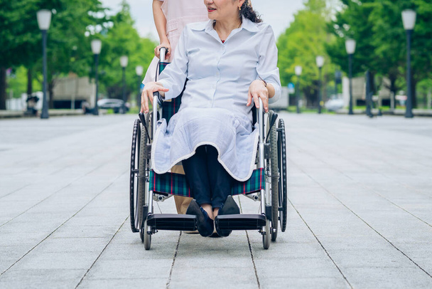 Eine Frau im Rollstuhl und eine Frau im Kittelschurz, die sich um draußen kümmert - Foto, Bild