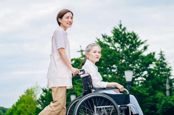 Une femme en fauteuil roulant et une jeune femme dans un tablier pour prendre soin de l'extérieur - Photo, image