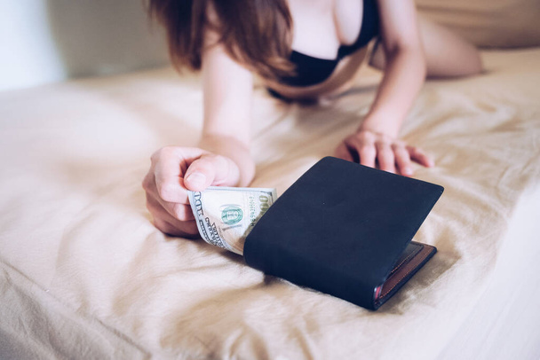 Обрезанный снимок молодой проститутки, крадущей деньги из кошелька клиента после окончания службы. Концепция проституции. - Фото, изображение