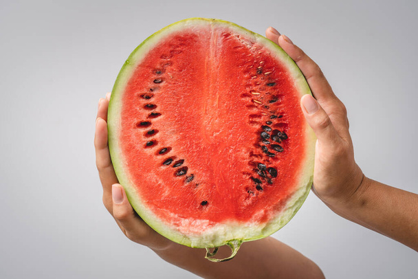 Half of watermelon in hands of unknown caucasian woman holding it in front of white wall background copy space - 写真・画像