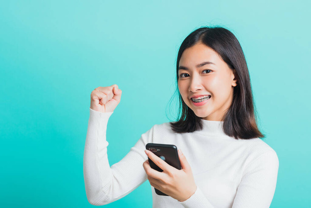 Asian woman smile holding smartphone she happy and surprised after received message, female excited cheerful her reading mobile phone some social media isolated on blue background, Technology concept - Foto, Imagem