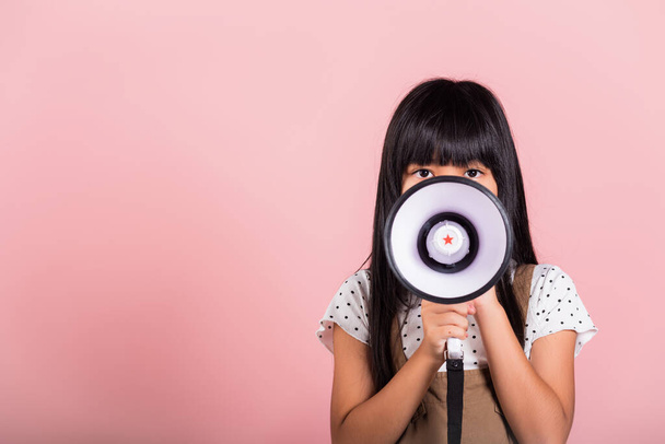 Asian little kid 10 years old shouting by megaphone at studio shot isolated on pink background, Happy child girl lifestyle she screeching through in megaphone announces discounts - Fotoğraf, Görsel