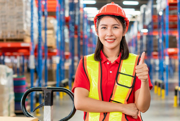 Χαρούμενη εργάτρια που δείχνει τους αντίχειρες της, χειρωνακτική εργάτρια στην αποθήκη, γυναίκα εργάτρια αποθήκης με τους αντίχειρες επάνω - Φωτογραφία, εικόνα