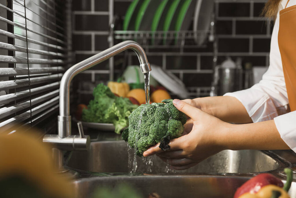 Ázsiai kéz nő mosás zöldség brokkoli és elkészítése egészséges étel a konyhában. - Fotó, kép