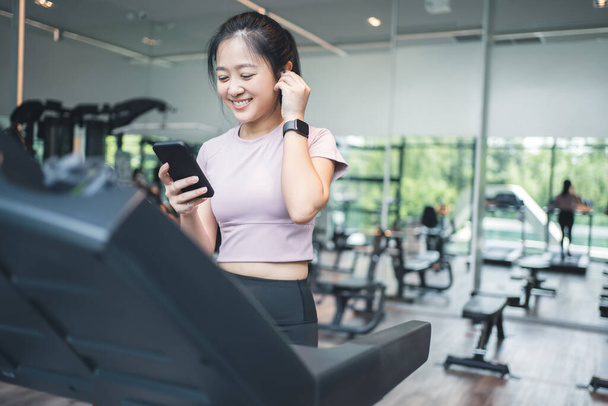 Portrait of an Asian woman exercising on a treadmill She is listening to music with wireless headphones and a smart watch. - Fotoğraf, Görsel