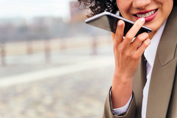 close up of the mouth of a smiling woman recording a voice message with a mobile phone, concept of communication and urban lifestyle, copy space for text - Foto, Bild