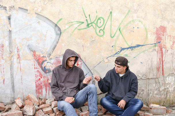 kaksi katuhuligaania tai räppäriä seisomassa graffitikipua vastaan
 - Valokuva, kuva