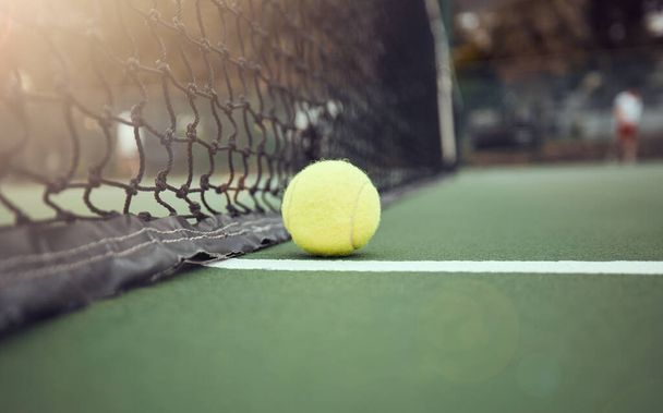 Closeup of one yellow tennis ball on the floor after hitting a net during a game on a court. Still life ball on a line during a competitive sports match in a sports club. Losing by touching the net. - Zdjęcie, obraz