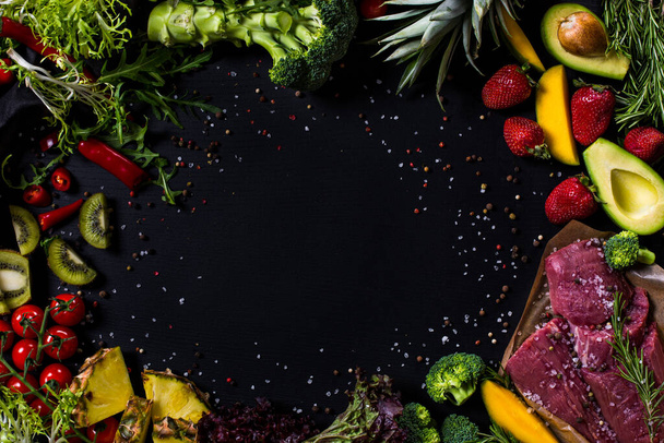 Black background with avocado, veal, herbs, strawberries, pineapple, cherry tomatoes, kiwi, broccoli and spices - Zdjęcie, obraz