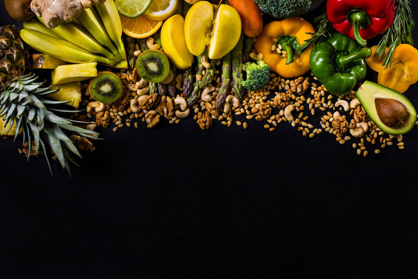 Schwarzer Hintergrund mit Walnüssen, Cashewnüssen, Pinienkernen, Paprika, Karotten, Brokkoli, Bananen, Ananas, Zitrusfrüchten, Ingwer und Kiwi - Foto, Bild