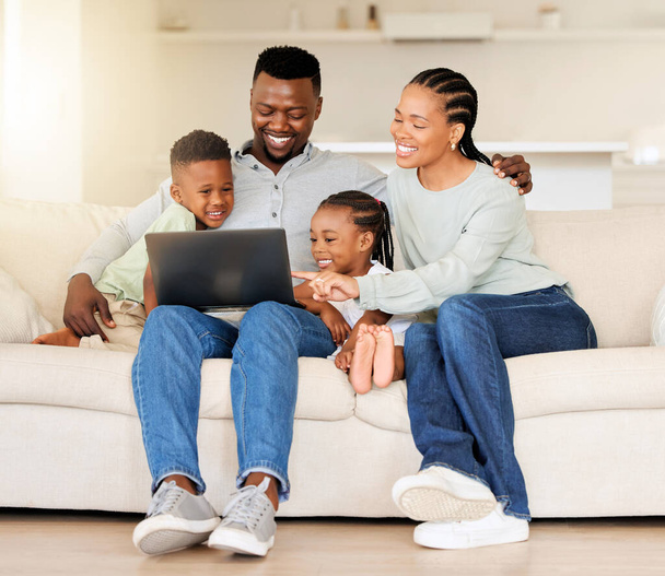 Boldog fiatal afro-amerikai család ül együtt és laptopot használ. Kíváncsi aranyos kislány és fiú ül a szüleikkel, és tanul videókat online. - Fotó, kép
