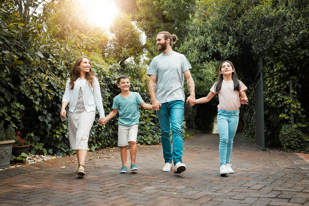 Happy young caucasian family of four holding hands and going for a walk in the neighbourhood. Carefree parents with their two children leaving their residence and going for a sunny stroll. - Photo, Image