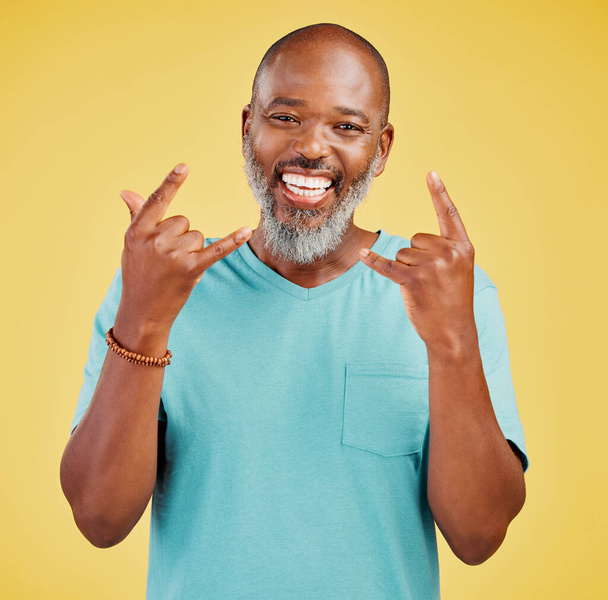 Porträt eines reifen freundlichen afrikanisch-amerikanischen Mannes, der glücklich und lächelnd aussieht, während er vor gelbem Studiohintergrund eine Geste mit der Hand macht. Ausdrücken, dass man feiern muss, um Rockmusik zu hören - Foto, Bild
