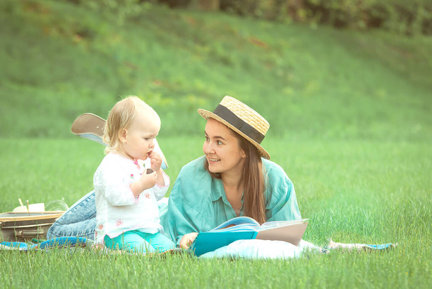 母は公園の芝生の上に寝そべっている赤ん坊の少女のための本を読んでいる。高品質の写真 - 写真・画像