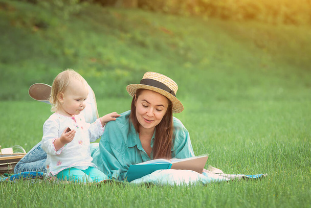Äiti lukee kirjaa tytölle, joka makaa nurmikolla puistossa. Laadukas kuva - Valokuva, kuva