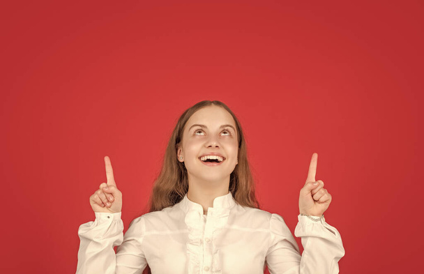 счастливый ребенок в белой рубашке указывая пальцем на красный фон копировать пространство, реклама. - Фото, изображение