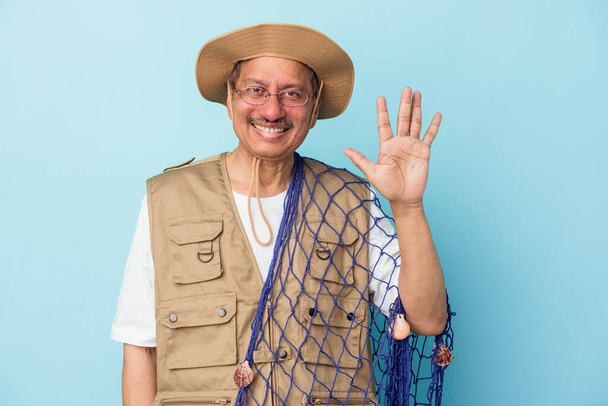 Senior indian fisherman holding net isolated on blue background smiling cheerful showing number five with fingers. - Photo, image