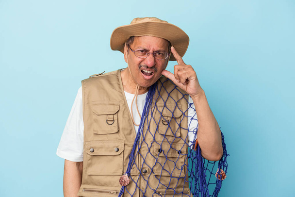 Senior indian fisherman holding net isolated on blue background showing a disappointment gesture with forefinger. - Foto, Imagem
